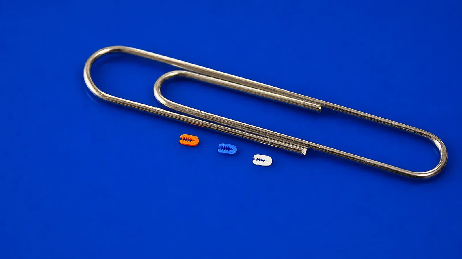 Tiny precision injection molded parts beside a paperclip for scale